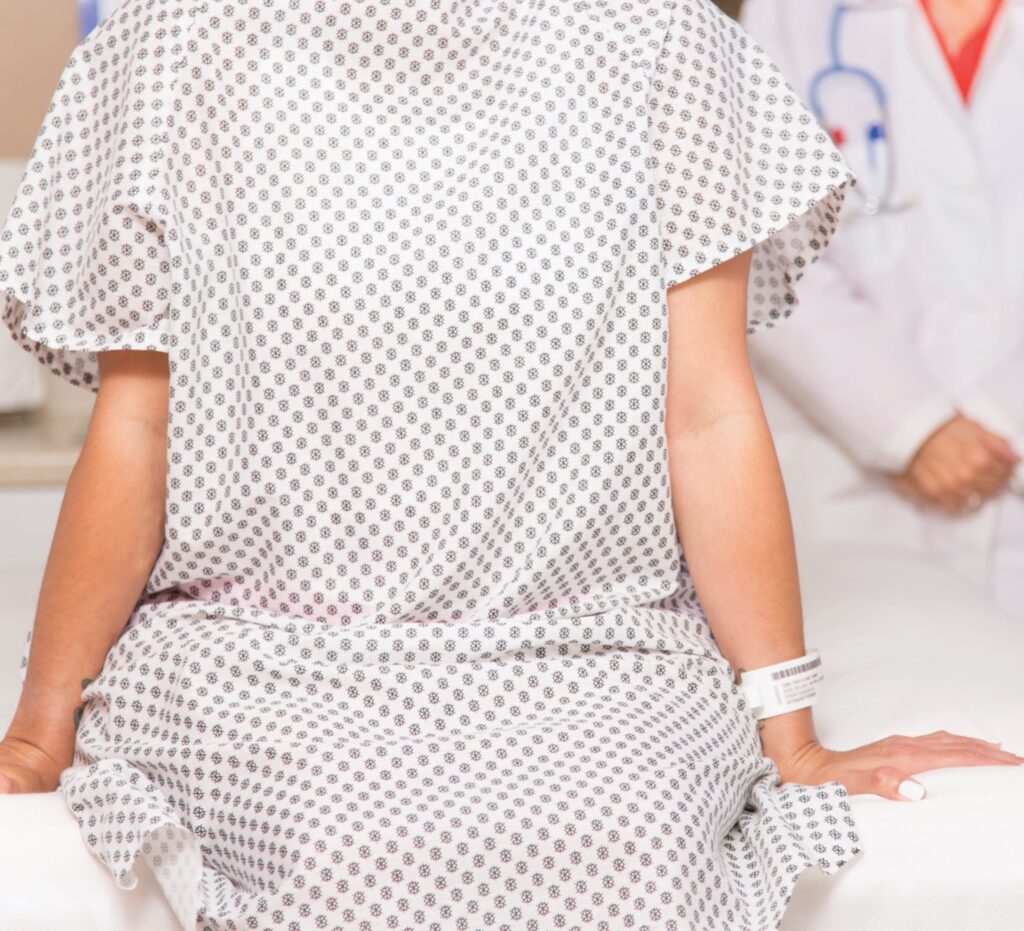 The image features a person wearing a white dress indoors. The dress has sleeve detailing and a patterned fabric.